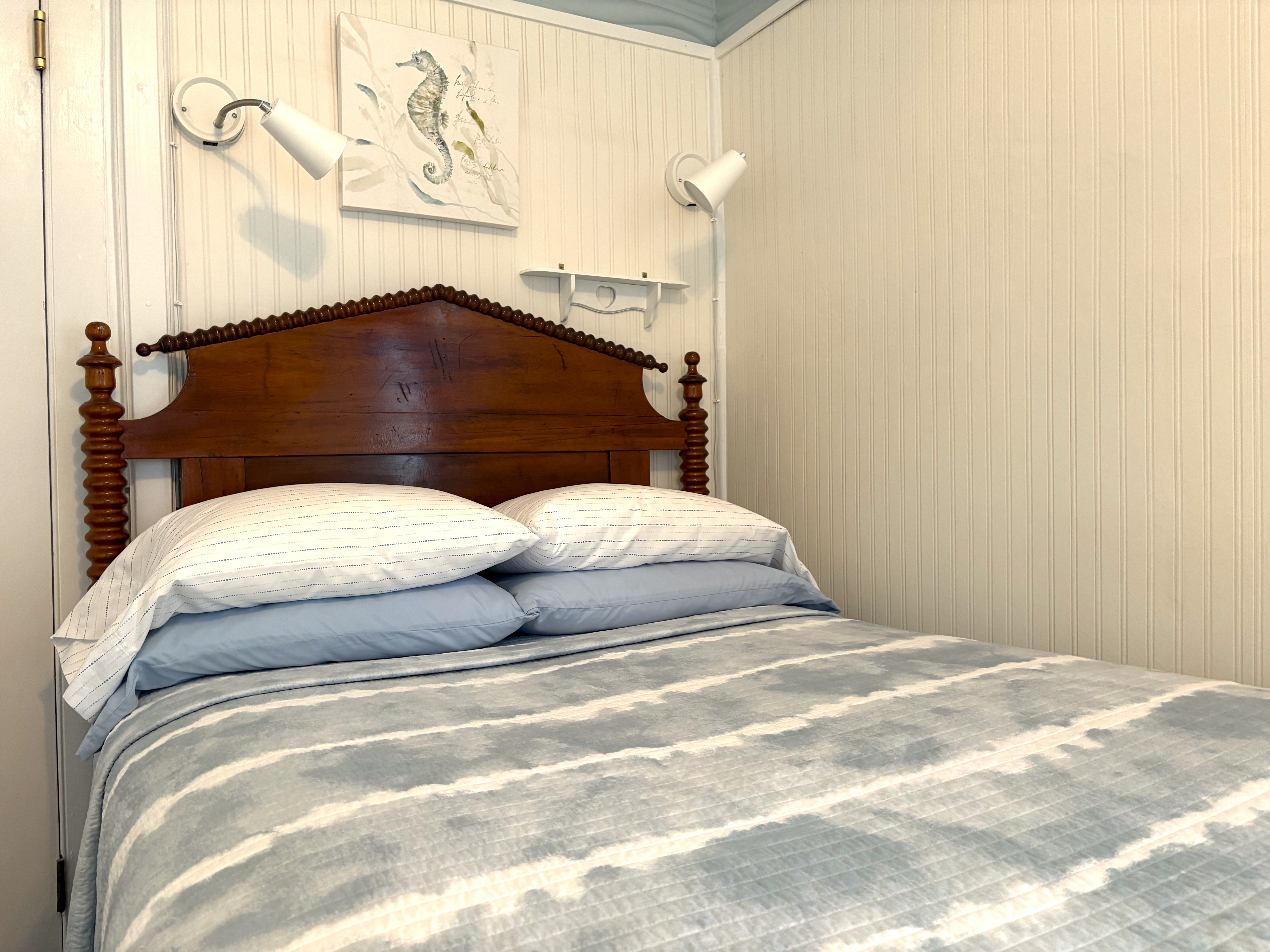 A cozy bedroom corner featuring a wood-frame bed with a blue and white striped comforter, a window with navy blue curtains, and a bedside table with a starfish-patterned lamp.