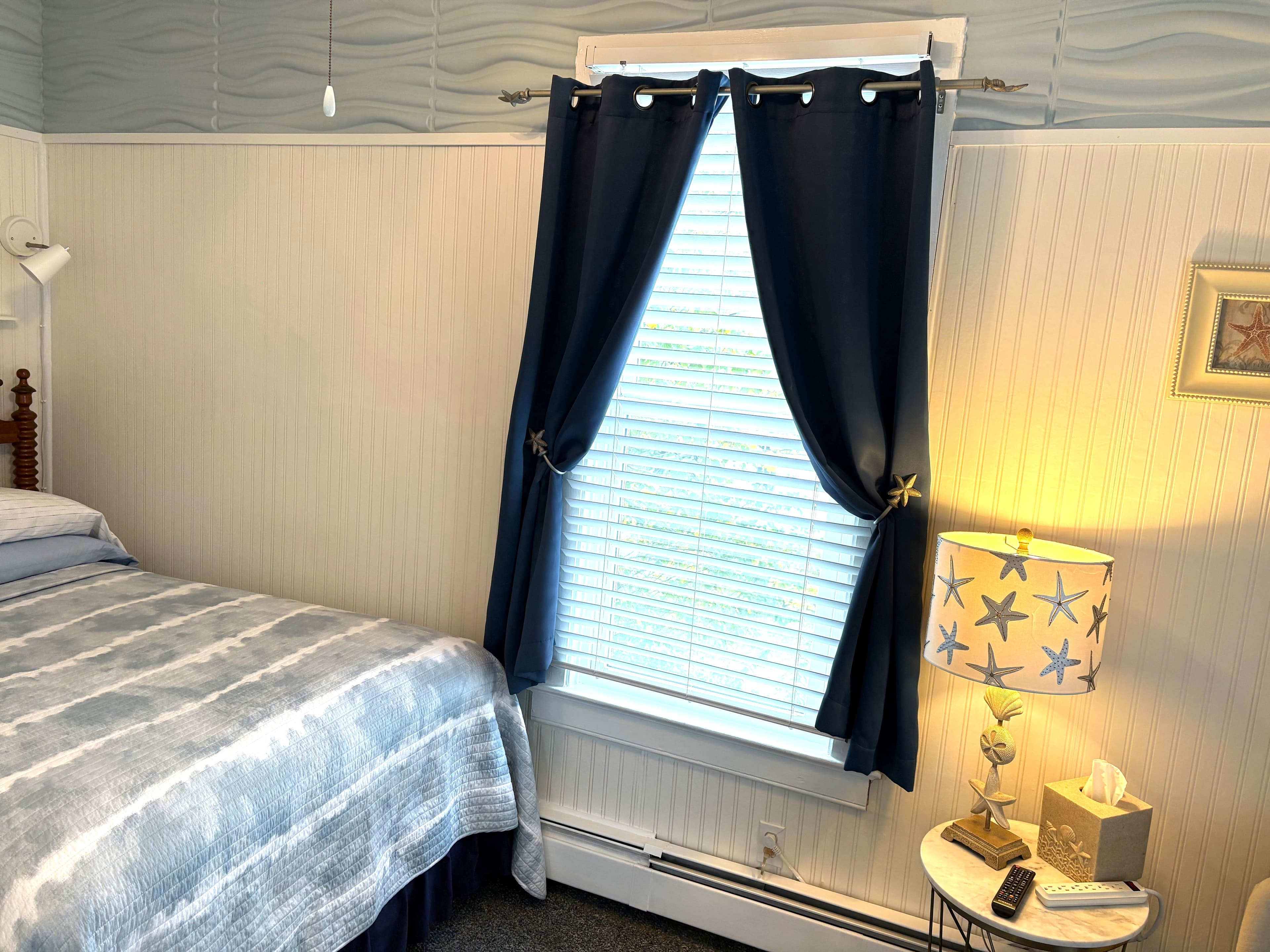 A carved oak bed with a blue and white striped comforter, set against a white beadboard wall featuring a seahorse painting and two white reading lamps.