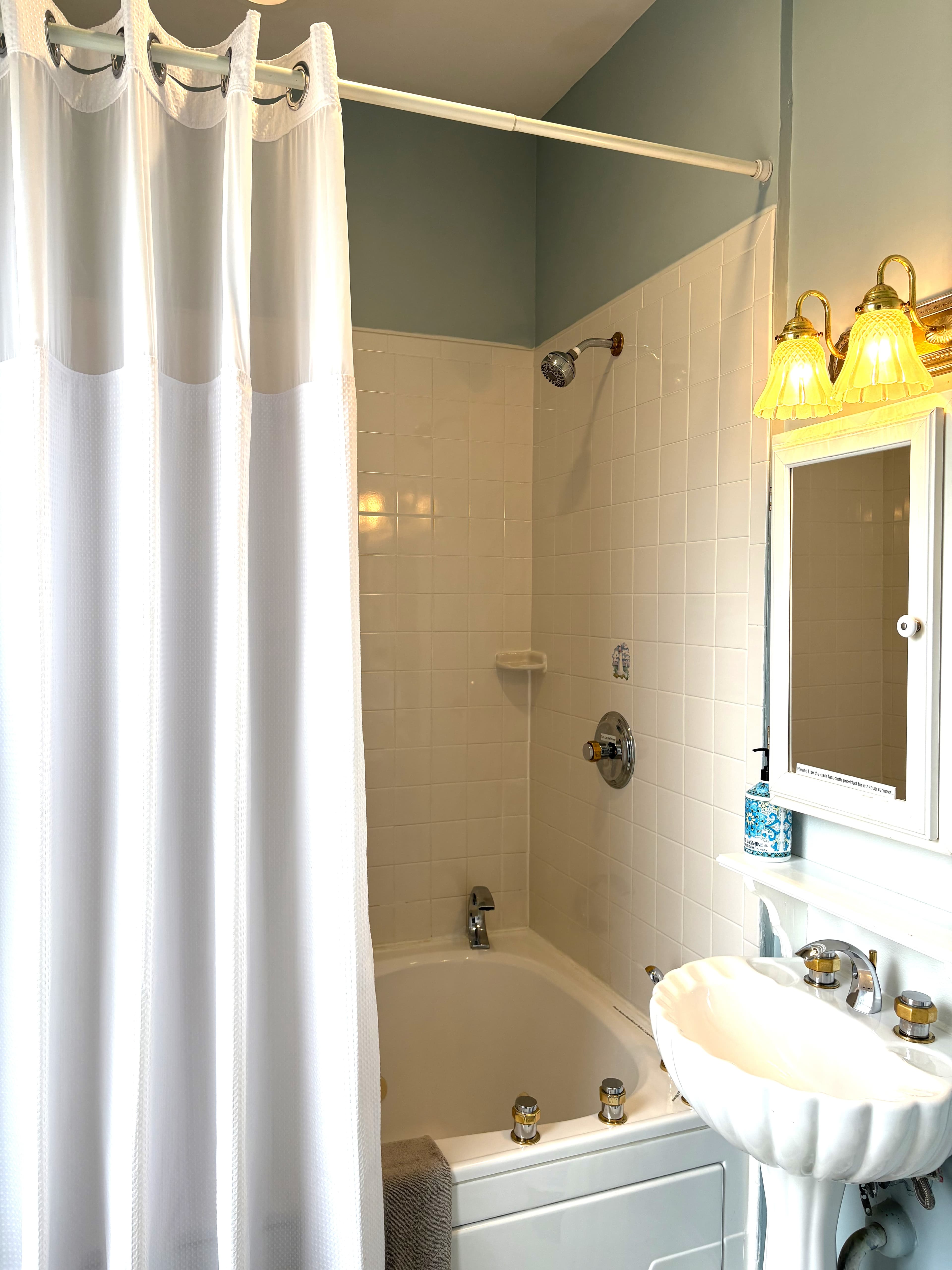 An interior view of a bathroom featuring a large watercolor-style painting of a blue mermaid on distressed wood panels, white and teal towels folded decoratively on a rack, and a wall-mounted hair dryer.
