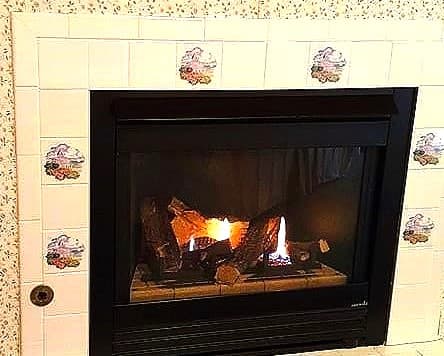 An interior view of a bedroom featuring a dark wood bed with blue and white patterned bedding. To the right is a large dark wood armoire, and an open door reveals a bright adjacent room.