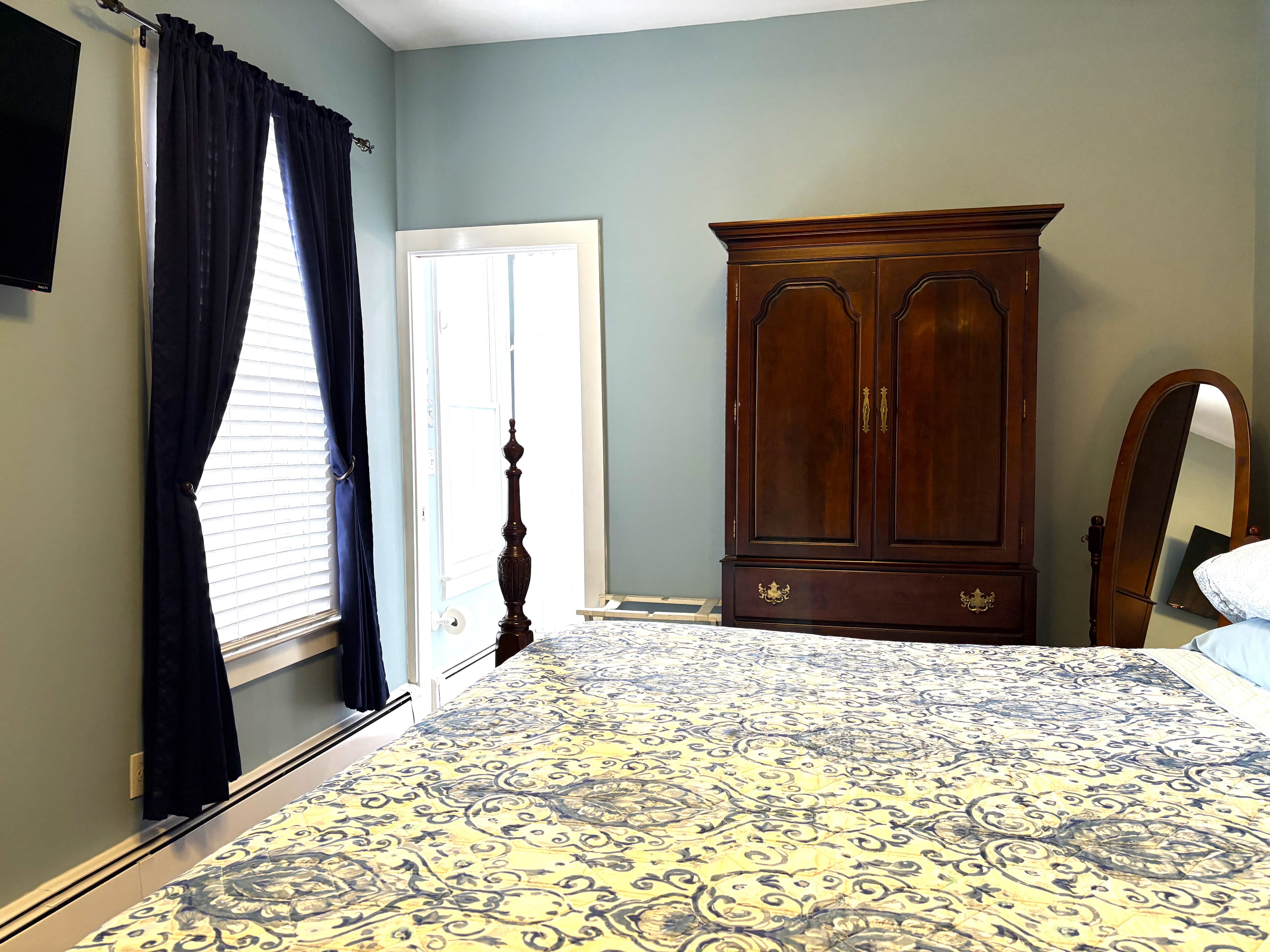 An interior view of a bright bathroom featuring a white Jacuzzi tub with a shower, a pedestal sink, and a mirrored medicine cabinet illuminated by warm wall-mounted lamps.