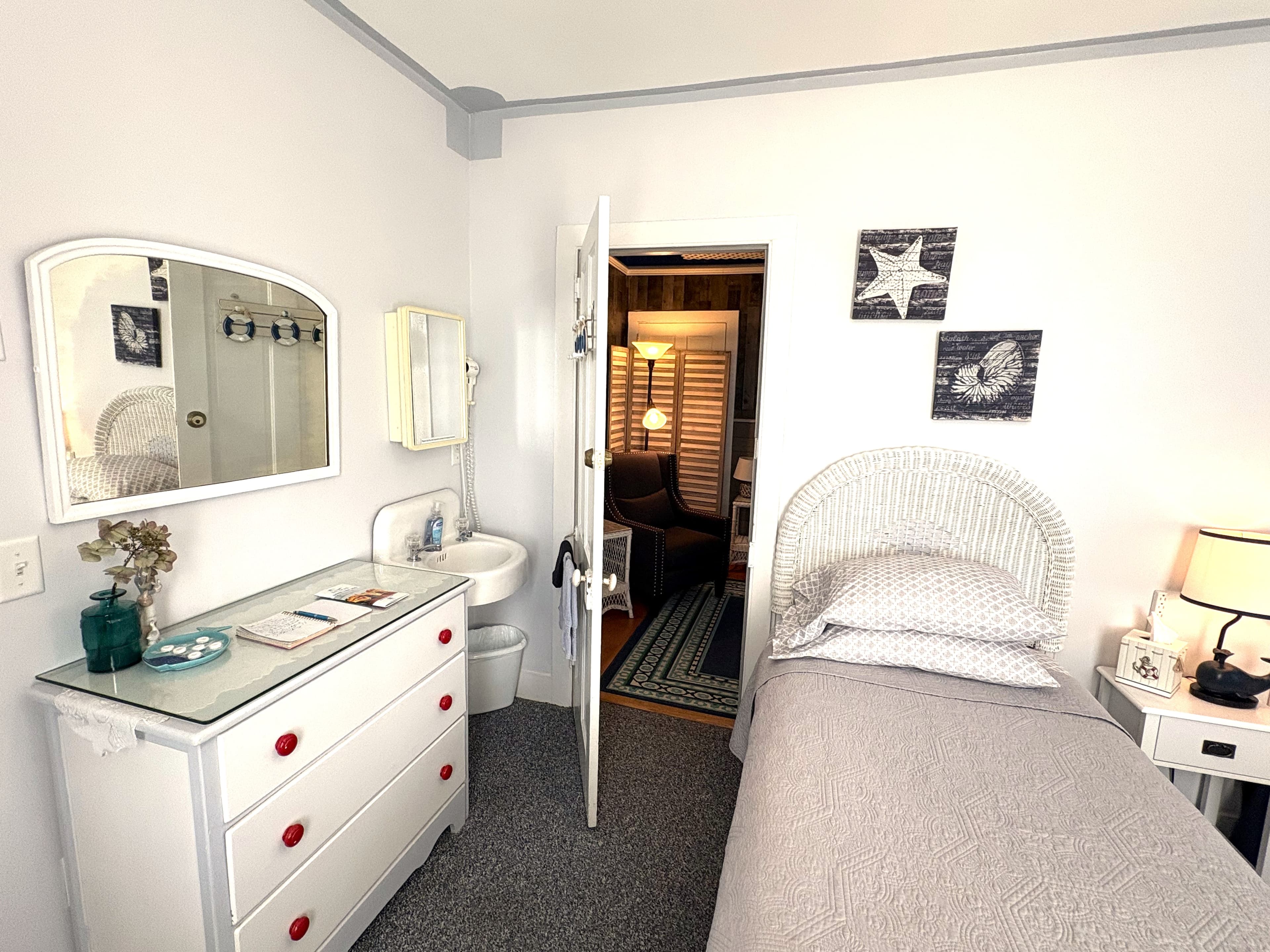An interior view of a cozy seating area featuring a dark gray sofa with decorative floral pillows, a large navy blue patterned area rug, and a tall bistro-style wooden table with two gray stools. The room includes a wall with rustic wood-paneling accents and navy blue curtains framing a window.