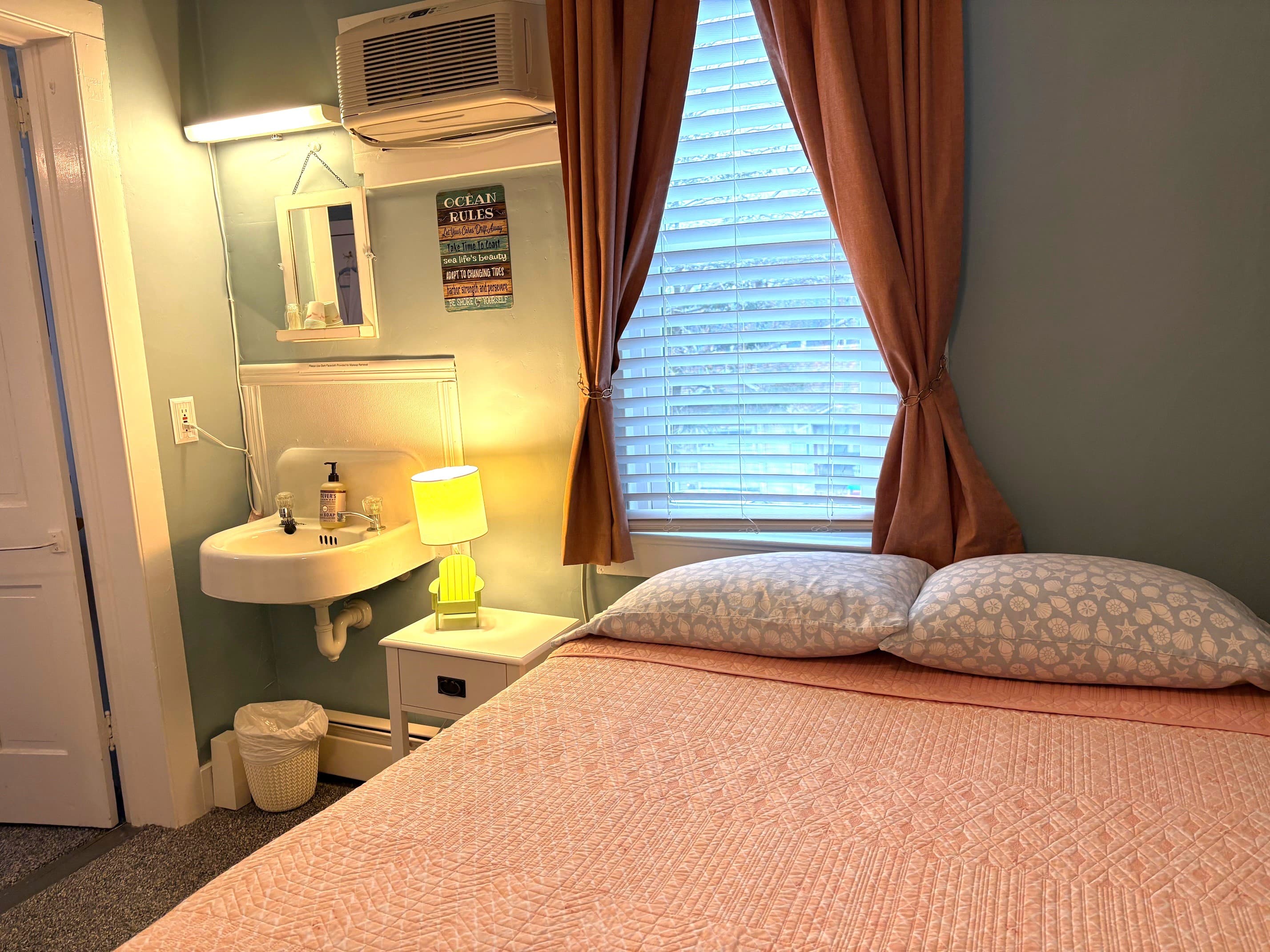 Cozy bedroom with an orange bedspread, a small sink, and a window with curtains.