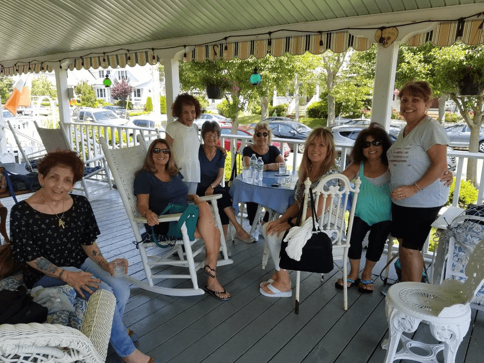 A group of eight women seated on a porch, talking and enjoying each other's company.