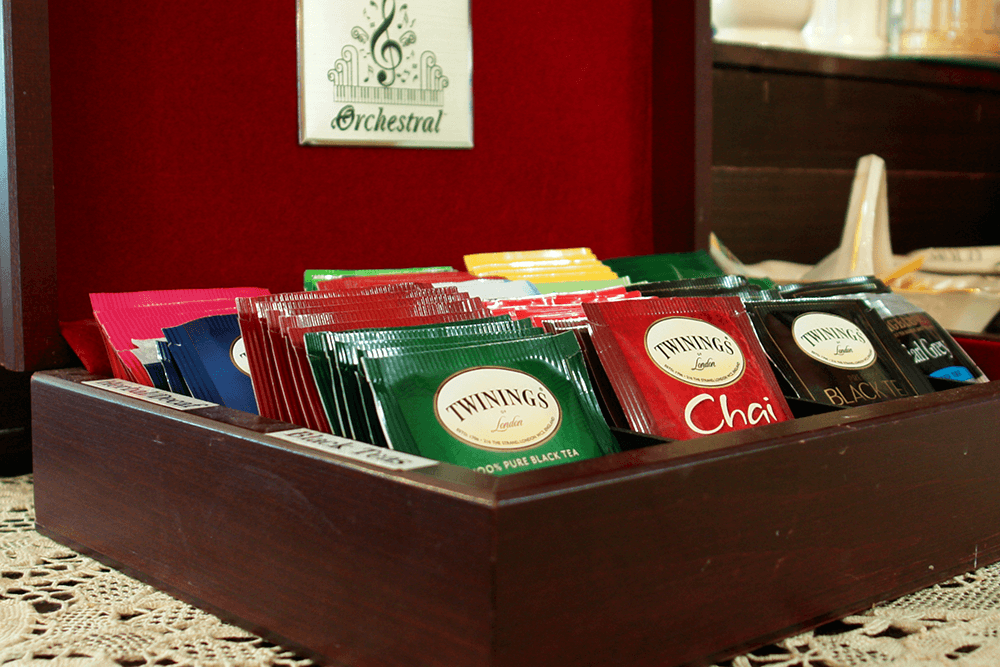 A wooden box filled with various Twinings tea bags in colorful packets.