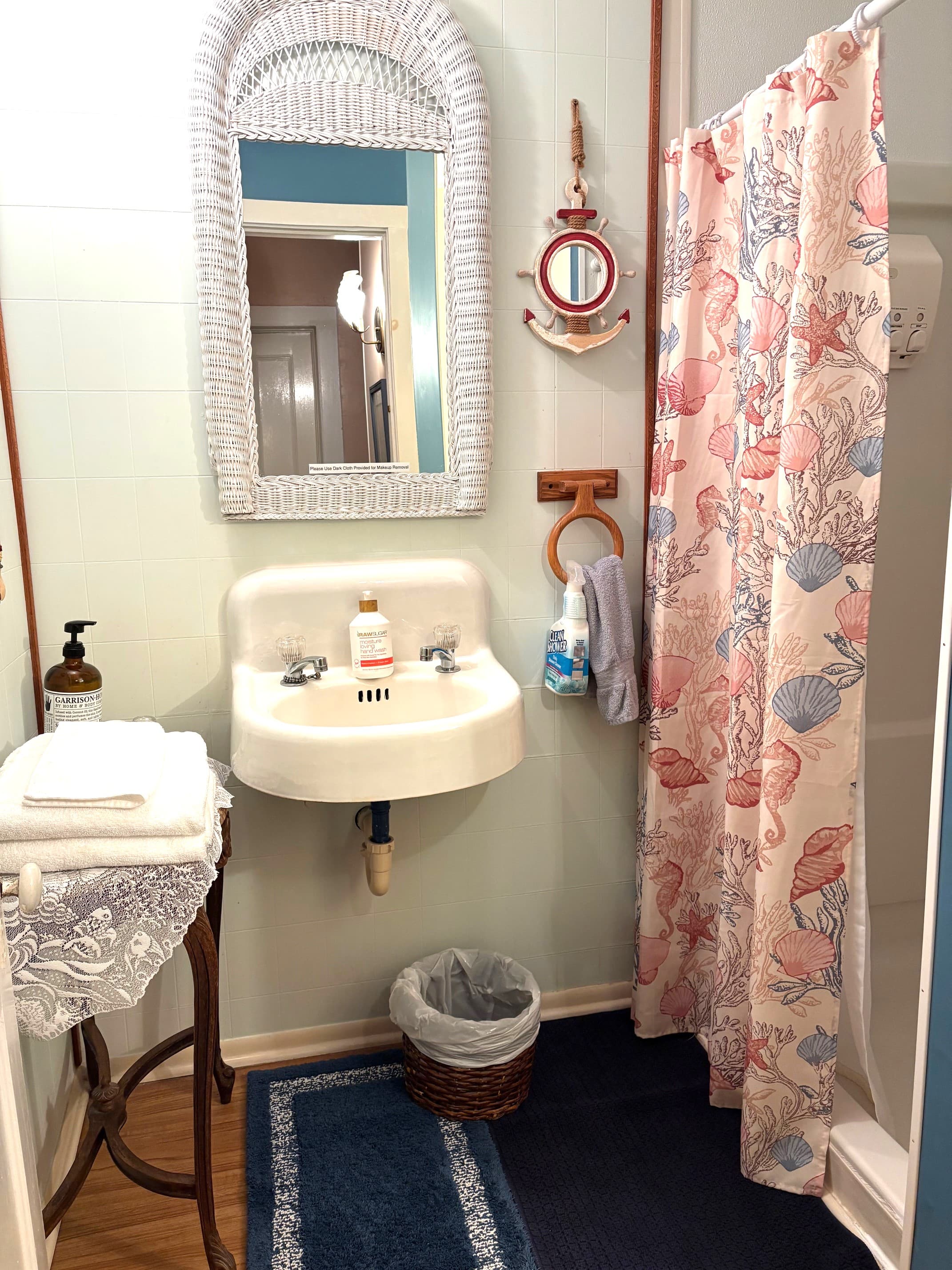 A quaint bathroom featuring a shell-patterned shower curtain, vintage sink, and decorative mirror.