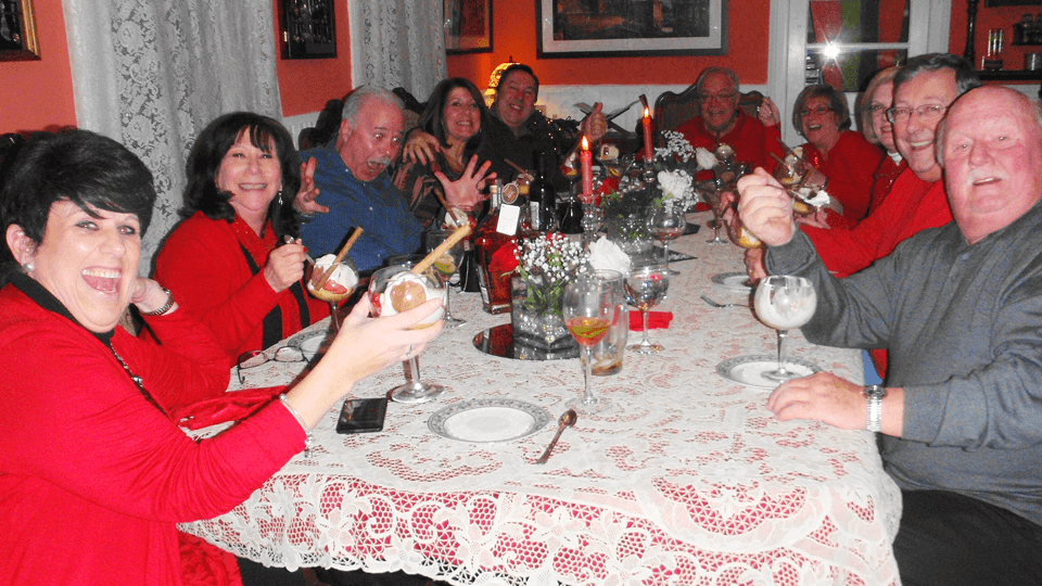 A group of cheerful friends in red attire gathers around a table, raising drinks and smiling at a festive dinner setting.