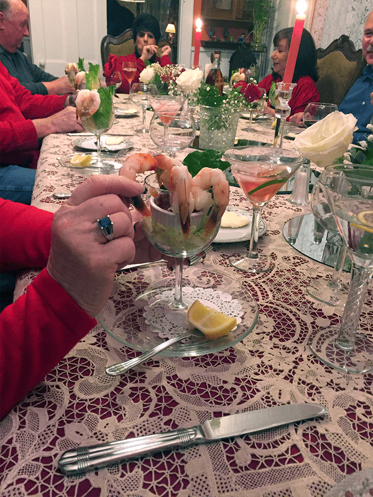 A festive dinner table with guests enjoying shrimp cocktails and cocktails amidst elegant decor and candlelight.