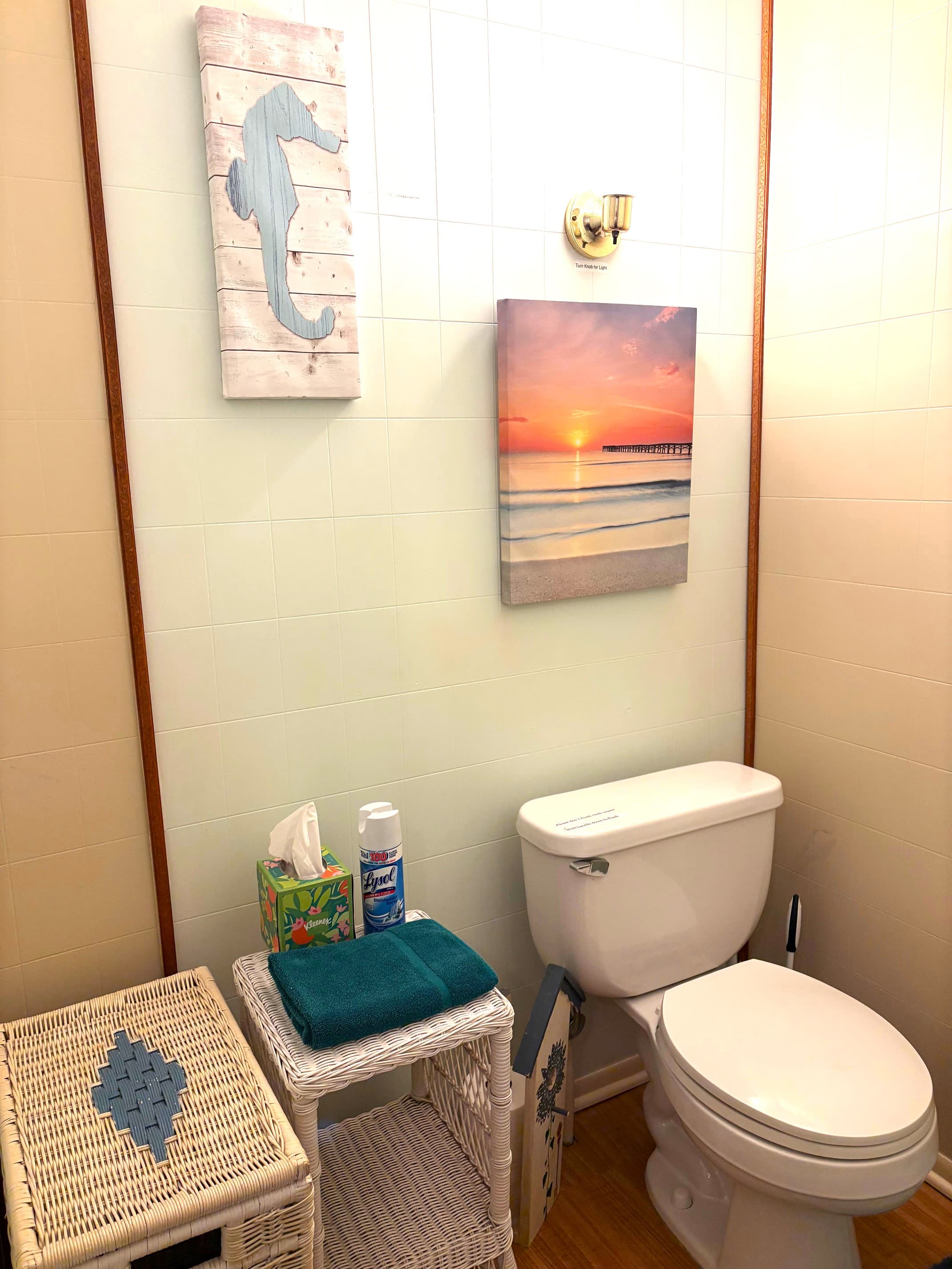 A compact bathroom featuring a toilet, decorative wall art, and a wicker storage unit.