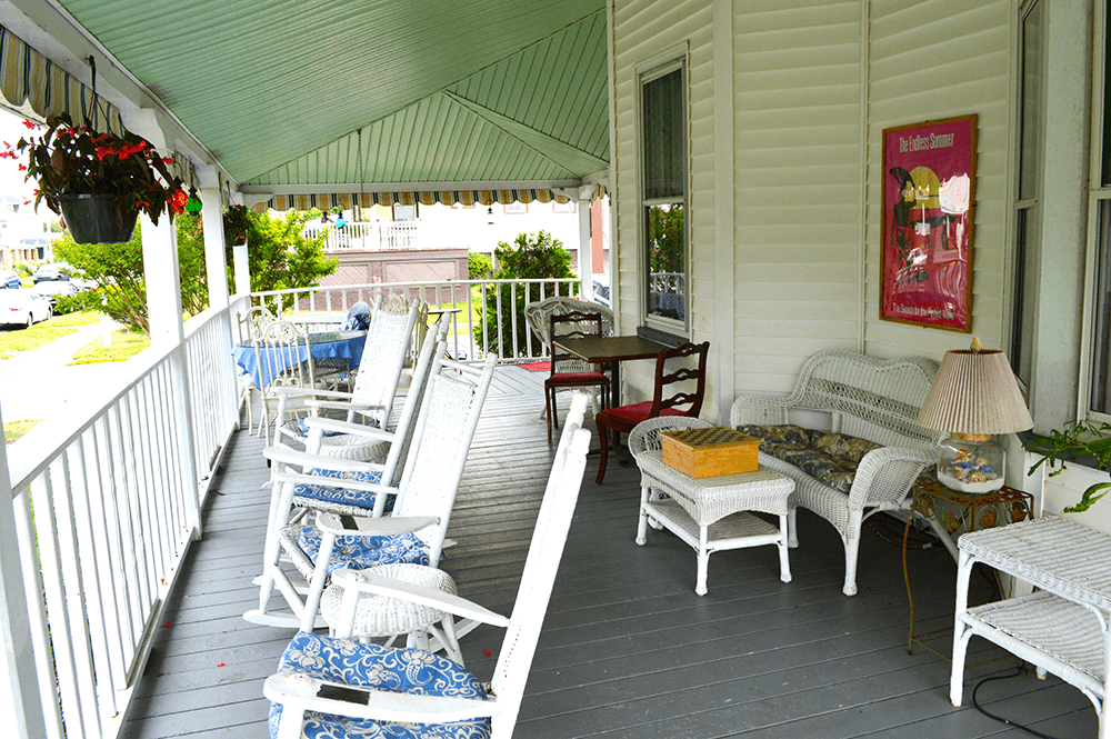 A spacious porch with white wicker furniture and blue cushions, surrounded by greenery.