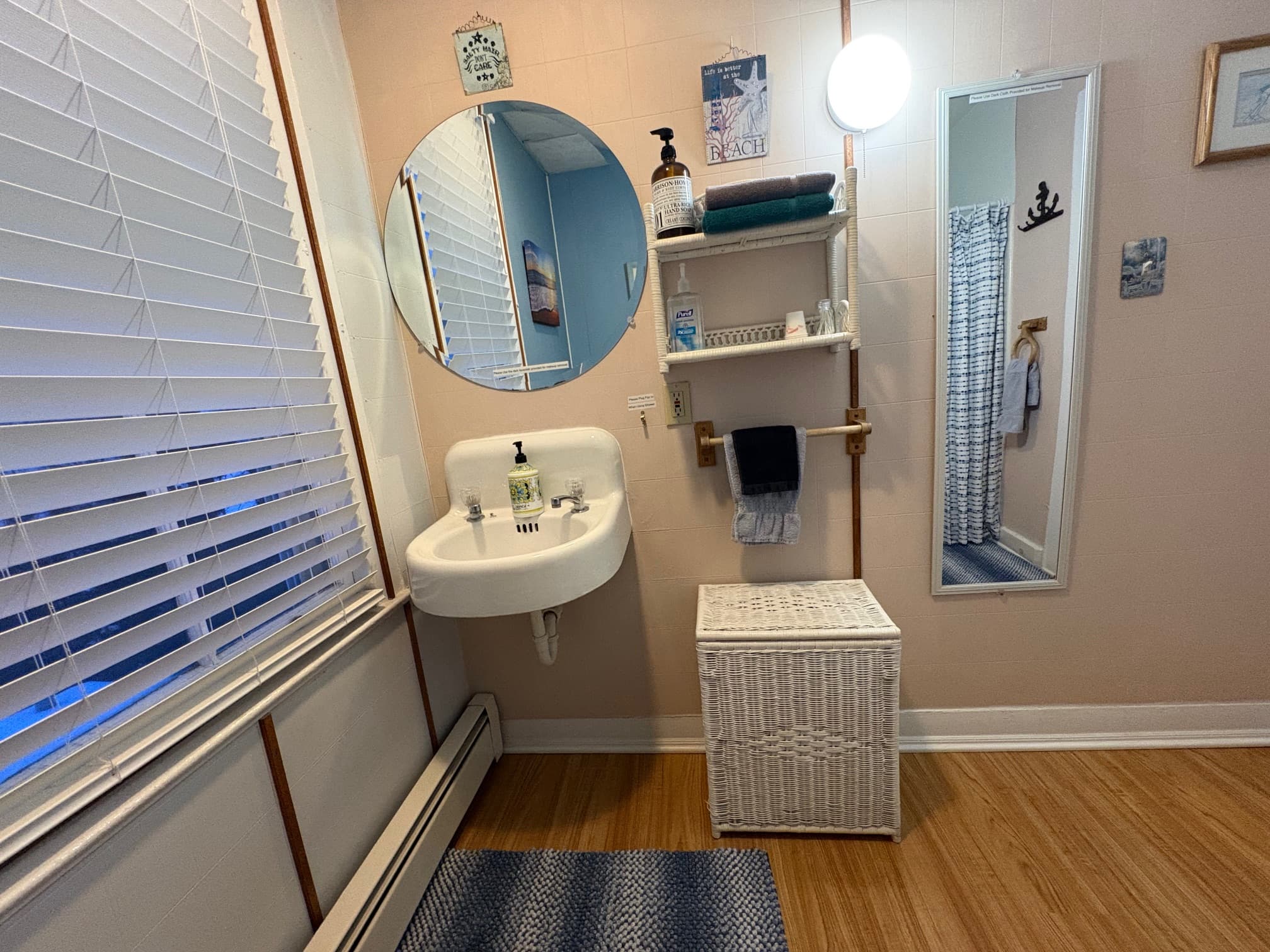 A bright, modern bathroom featuring a circular mirror, wall shelves with toiletries, a sink, and a wicker storage basket.