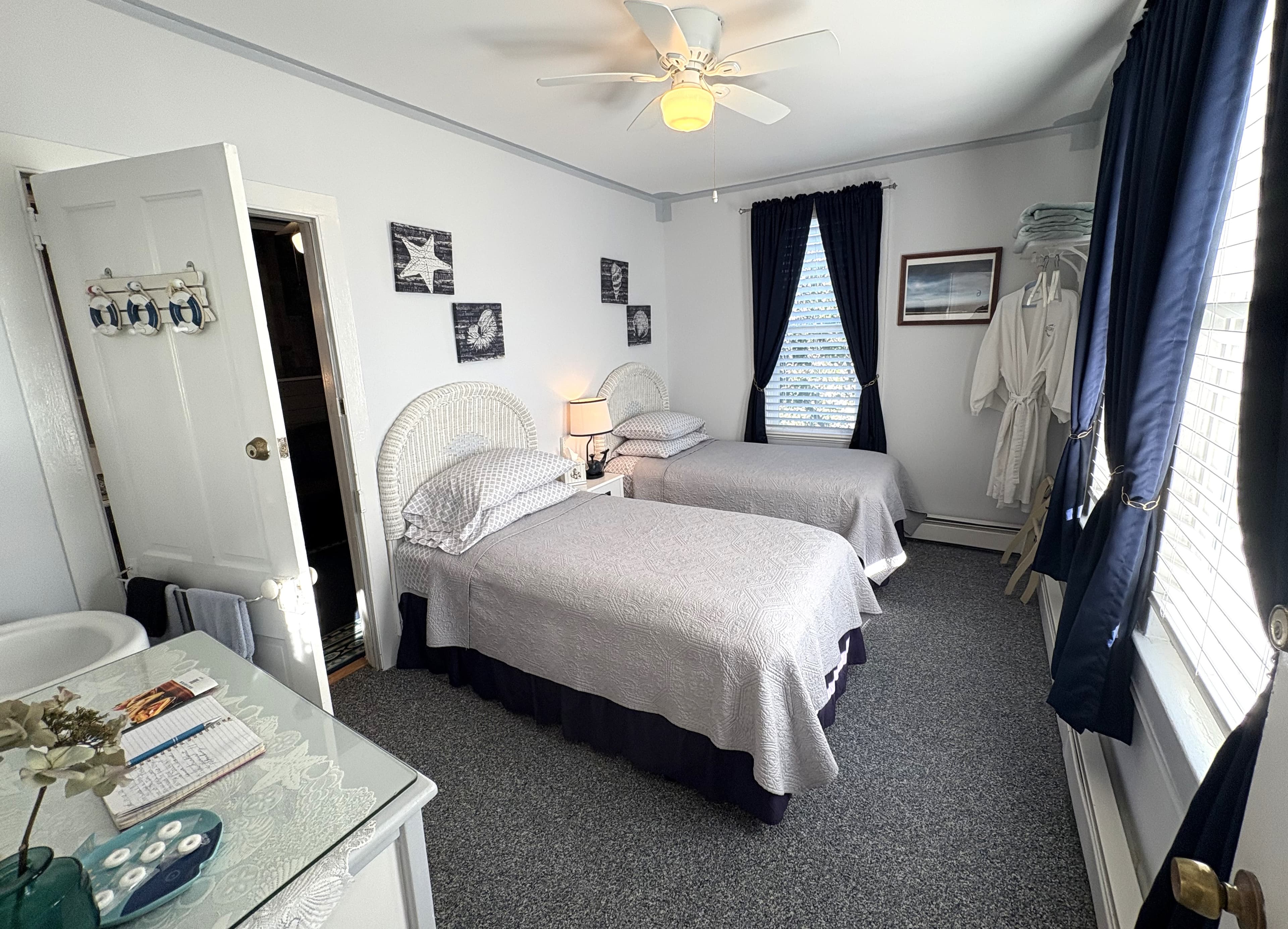 A cozy bedroom featuring two twin beds, a ceiling fan, and nautical-themed decor.