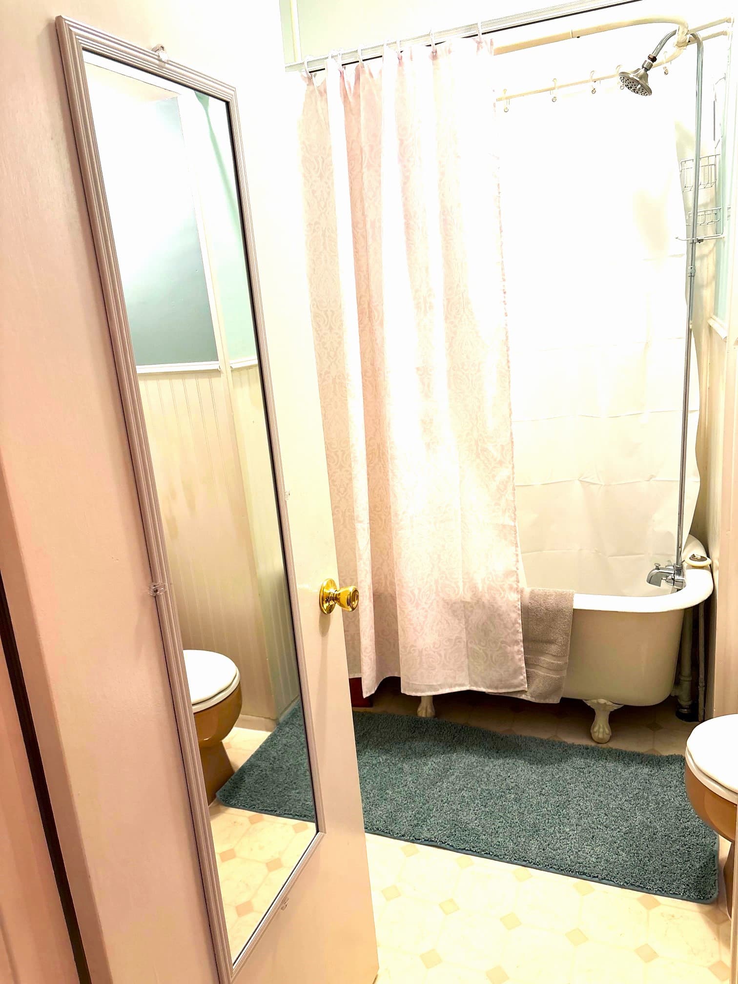 A small bathroom featuring a shower curtain, bathtub, toilet, and a mirror on the door.
