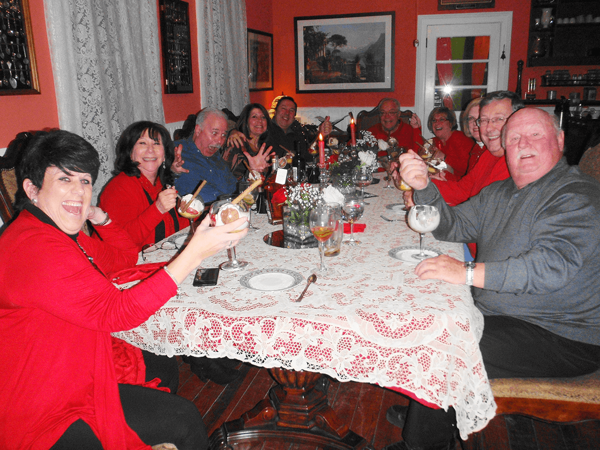 A group of people in red outfits joyfully celebrating around a decorated dining table with drinks.