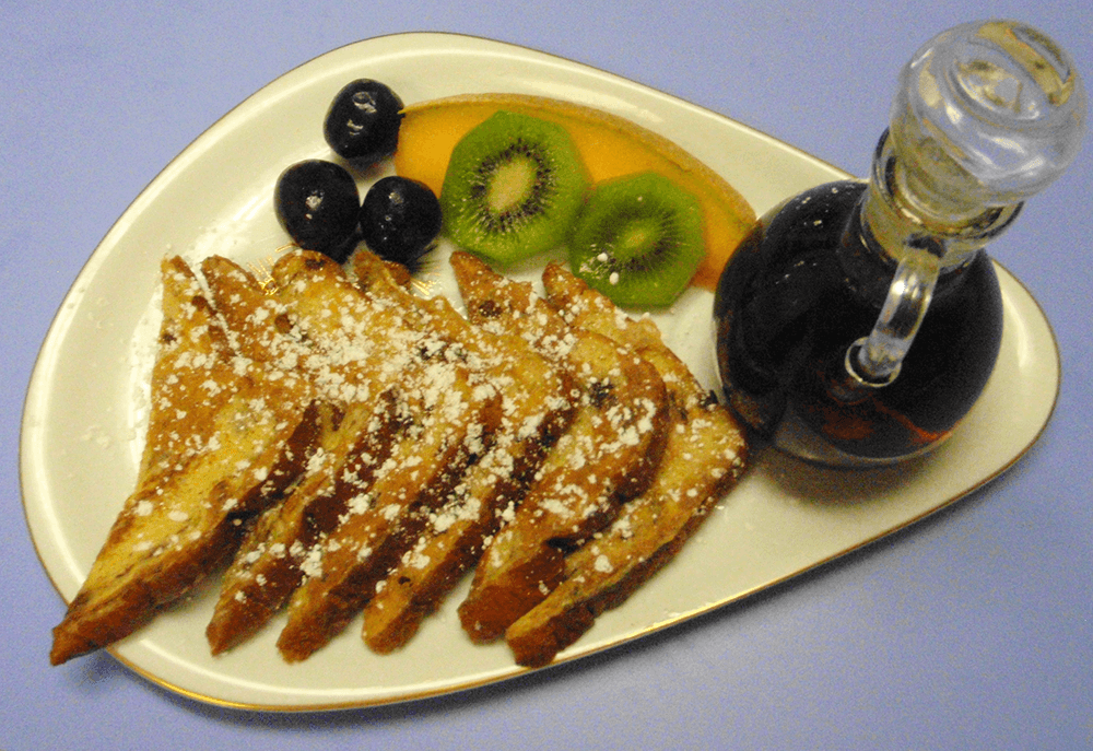 A plate of French toast sprinkled with powdered sugar, accompanied by fruit slices and syrup.