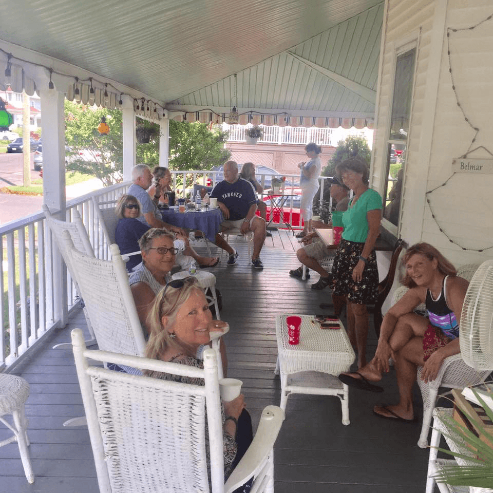 A group of people relaxes on a porch, sitting on rocking chairs and enjoying drinks.