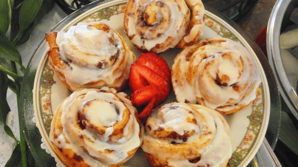 A plate of five frosted cinnamon rolls accompanied by a fresh strawberry.