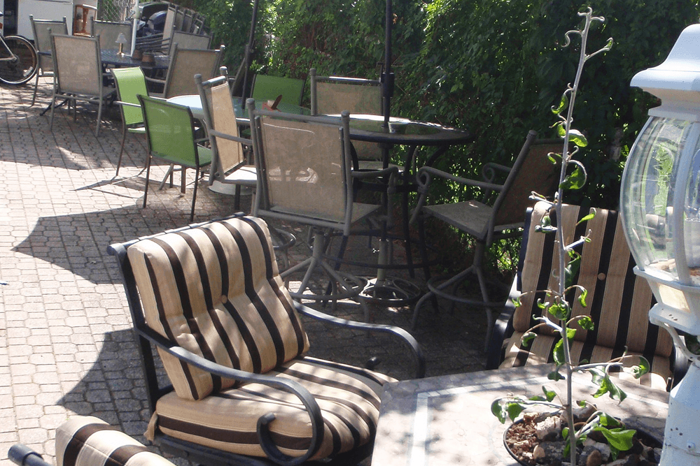 A sunlit outdoor seating area with striped lounge chairs and several metal tables surrounded by greenery.