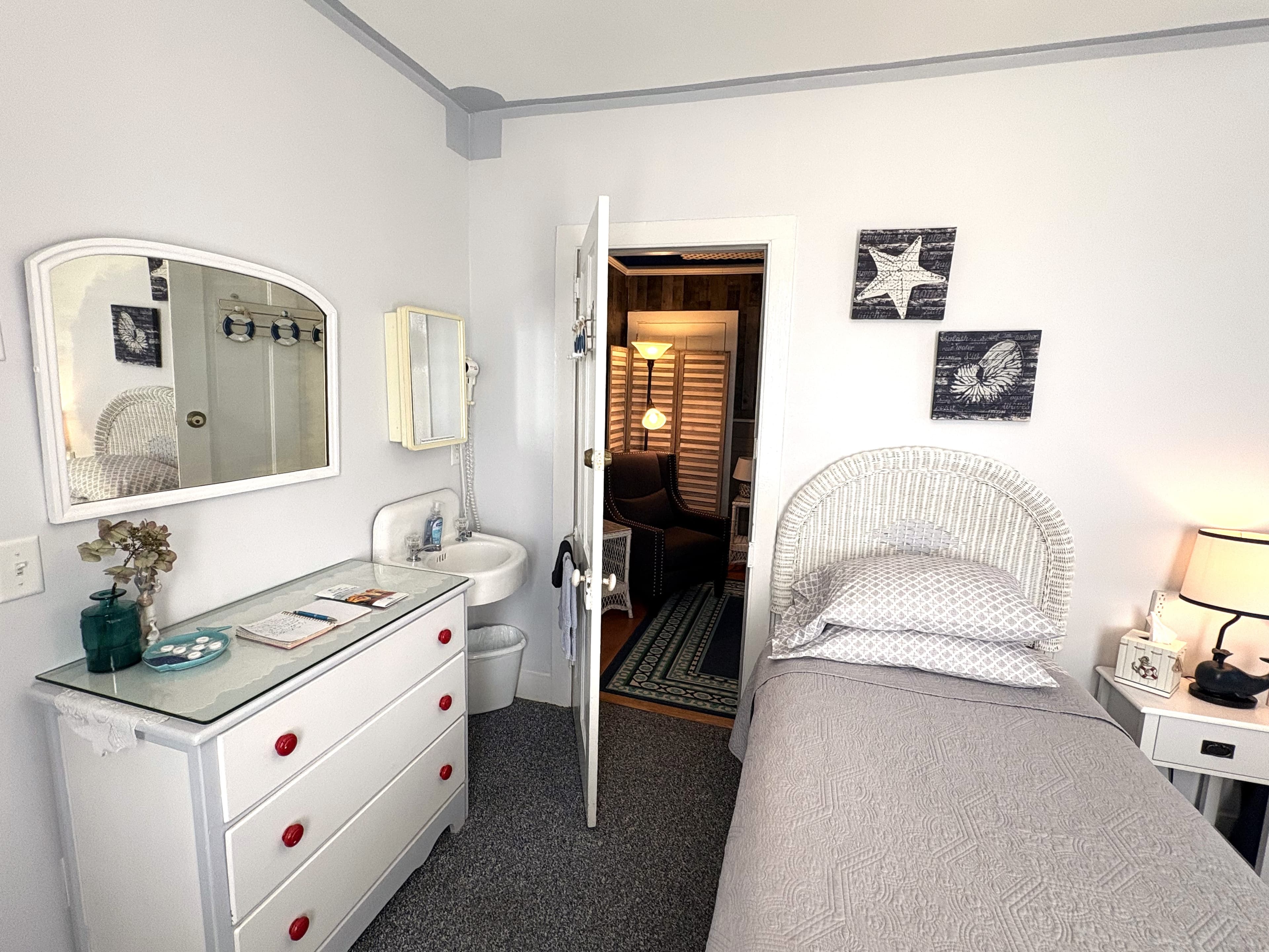 A cozy bedroom featuring a single bed, a white dresser with red knobs, a mirror, and an open door leading to another room.